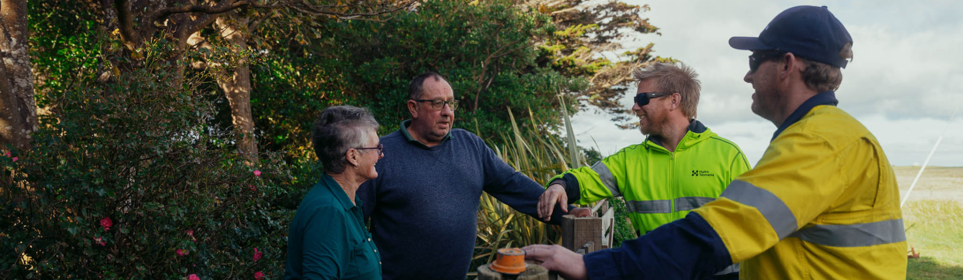 Two Hydro workers speaking to two community members in the front garden of their home