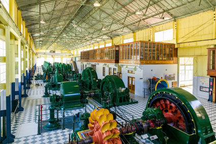 The Waddamana power station floor, with tiles floors alternating white and green. Large green turbines with red and yellow accents rise up from the floor, in a line through the power station. The internal walls are yellow.