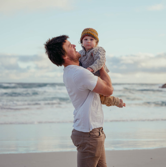 Person holding their young child up in an embrace, on a beach