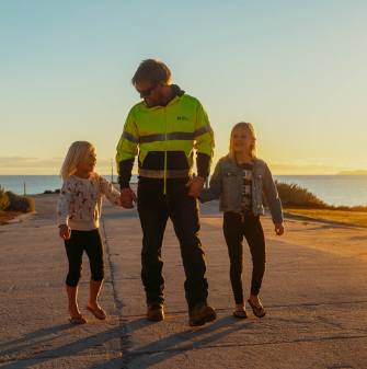 Hydro employee wearing high-vis walking with his two children with sunset in the background