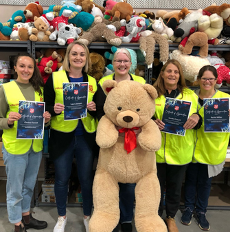 A group of Hydro Tas employees smiling with participation certificates from volunteering at Christmas time, with children&#39;s toys in the background