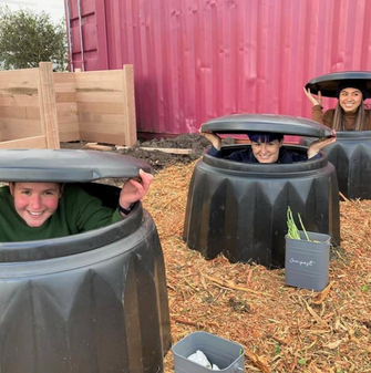 Three people sitting inside compost bins smiling at the camera