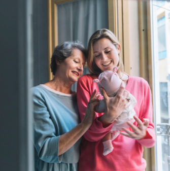 A mum embracing their young infant, with a grandmother overlooking