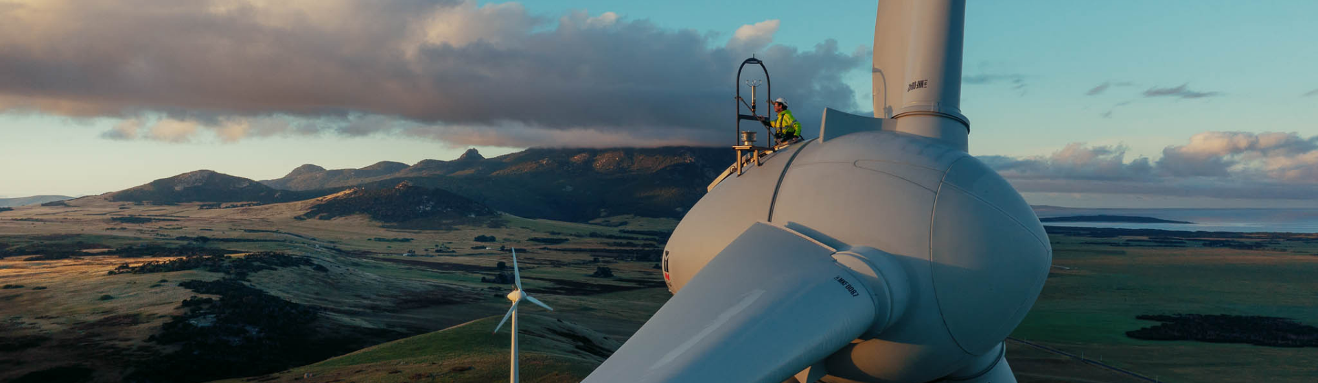 A Hydro employee working on a wind turbine in the foreground, with a second wind turbine in the background, on King Island