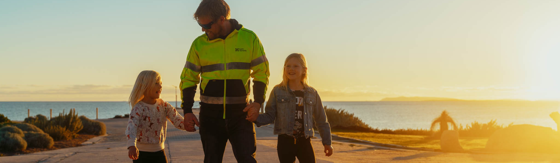 Hydro employee in high-vis walking alongside his two children with sunset in the background